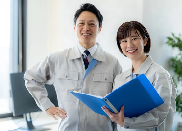 作業服を着た男女のスタッフが笑顔で打ち合わせをしている様子