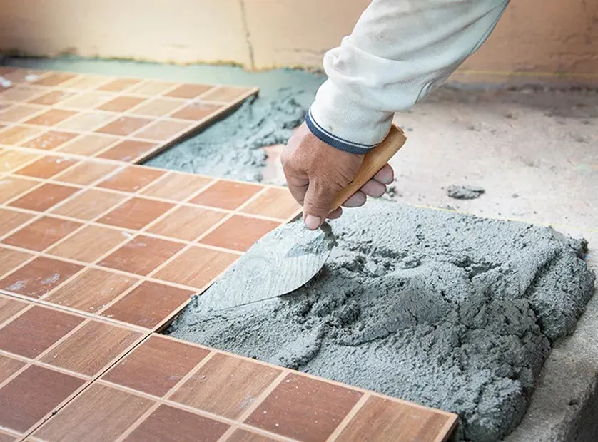 職人がコテを使ってセメントを敷き、床タイルを施工している様子