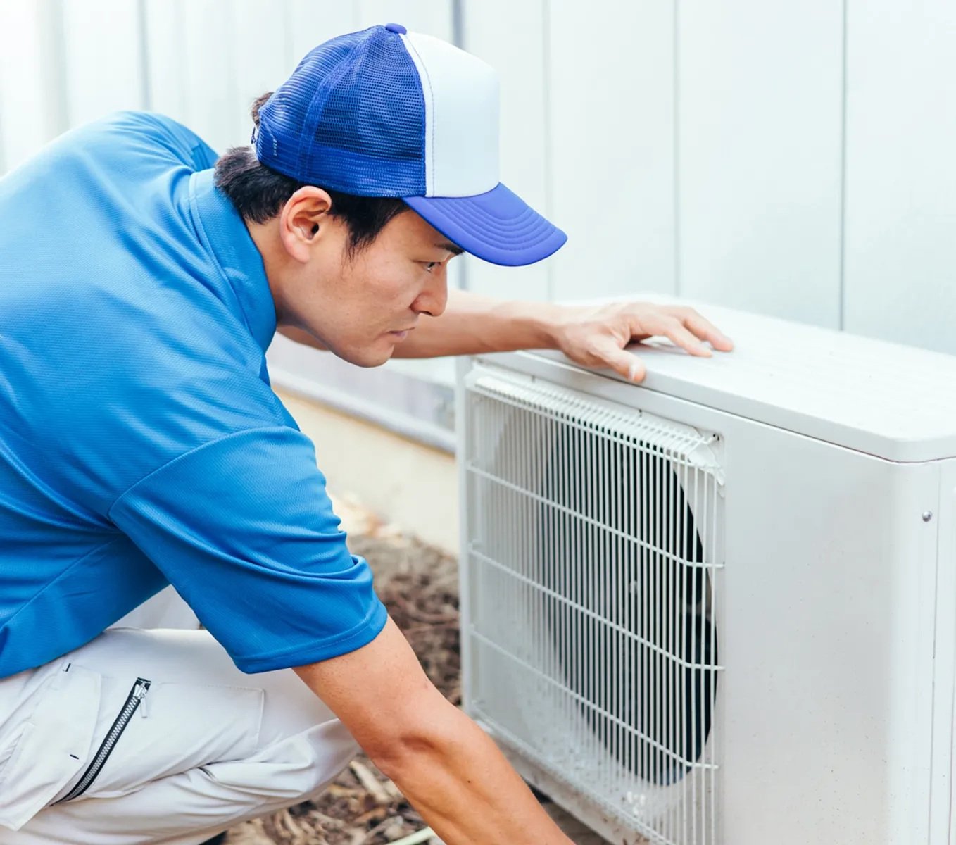 青い作業着の男性が室外機を点検している様子
