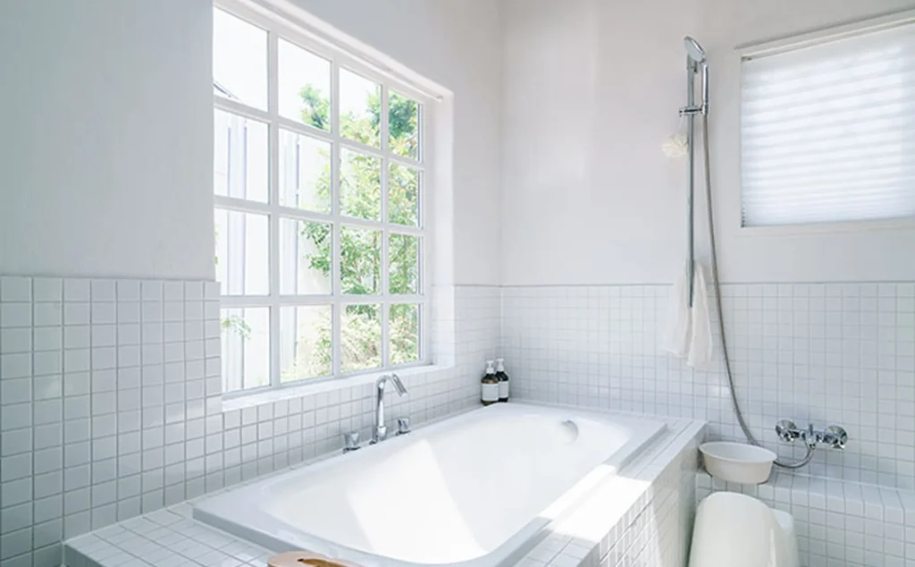 大きな窓から光が差し込む白タイル張りの浴室